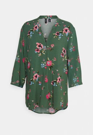 Blusa floreale verde con scollo a V, maniche 3/4, caratterizzata da fiori rosa e blu su un tessuto morbido. Design fluido e orlo arrotondato.