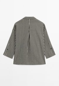 Veste à rayures noir et blanc avec des manches trois-quarts, arborant un col classique et un pli au centre à l'arrière pour plus de structure.