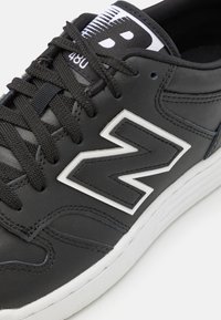 Adidași negri din piele cu accente albe. Prezintă un logo alb „N” proeminent, șireturi negre și un material superior texturat. Talpă din cauciuc.