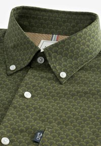 Green patterned shirt with a leaf design, featuring a collared neckline, white buttons, and a small logo on the front pocket.