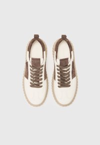 Baskets blanches avec des accents en daim marron. Design à lacets, semelle en caoutchouc avec une épaisse rainure. Logo subtil sur la languette, forme de bout arrondi.