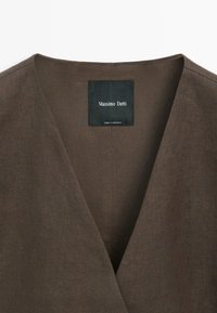 Hnědý lněný oděv s výstřihem do V a černou etiketu s nápisem "Massimo Dutti Made in Morocco" přišitou uvnitř límce.
