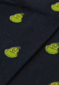 Mørkeblåt stof med flere grønne Grinch ansigtstryk. Materialet er strikket med en blød tekstur. Designet inkluderer detaljerede ansigtsudtryk.