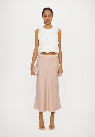 Weißes ärmelloses Crop-Top mit floralem Stickdesign, kombiniert mit einem enganliegenden rosa Midirock. Klare Sandalen mit Absatz runden den Look ab.