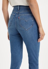 Jeans de mezclilla azul de cintura alta con un diseño de bolsillo trasero en forma de corazón y textura suave, con una silueta ajustada y costuras clásicas.