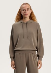 Brązowa bluza z kapturem o luźnym kroju, z możliwością regulacji sznurka, z ryflowanym dołem i mankietami. Posiada gładką teksturę i jest połączona z dopasowanymi spodniami dresowymi.