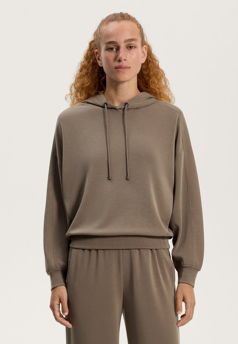 Brązowa bluza z kapturem o luźnym kroju, z możliwością regulacji sznurka, z ryflowanym dołem i mankietami. Posiada gładką teksturę i jest połączona z dopasowanymi spodniami dresowymi.