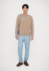 Šviesiai rudo vilnonio megztinio, šviesiai mėlynų dryžuotų kelnių, rudų raištelių batų ir mažos mėlynos petnešos derinys. Paprasta, laisva forma ir tinkantis dydis.