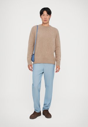 Šviesiai rudo vilnonio megztinio, šviesiai mėlynų dryžuotų kelnių, rudų raištelių batų ir mažos mėlynos petnešos derinys. Paprasta, laisva forma ir tinkantis dydis.