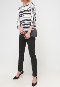 Blouse à rayures noires et blanches avec des manches trois-quarts, associée à un pantalon slim noir et des escarpins noirs à bout pointu. Pochette noire à la main.