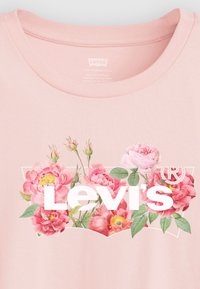 Ljusrosa t-shirt med ett blommönster som har rosa rosor. Grafiken inkluderar "Levi's"-logotypen i vitt i mitten.