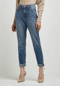 Jeans de mezclilla azul de talle alto con pierna recta, sutil desgaste, bajos remangados, diseño de cinco bolsillos y cierre con botón metálico.