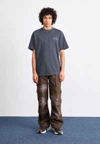 T-shirt cinza de manga curta com o texto "Nike" em roxo, combinado com calças cargo castanhas com múltiplos bolsos e um corte descontraído.