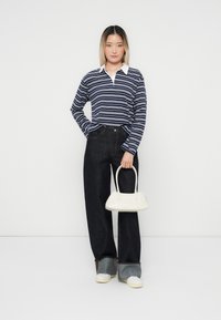 Marine- og hvitstripet langermet polo, mørke vide jeans, hvit håndveske og kremfargede sneakers; glatt stoff og tydelig fargekontrast.