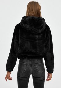 Sudadera corta negra hecha de suave pelo sintético, con capucha, corte relajado y dobladillo elástico. Combinada con jeans oscuros ajustados.