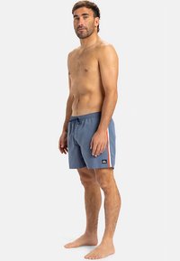 Pánske plavky v svetlo modrej farbe s elastickým pásom, s bočným prúžkom v oranžovej farbe a logom na ľavej nohe.