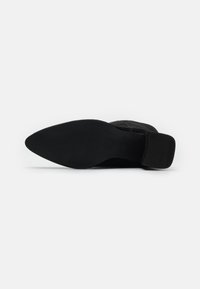 Sorte semskede ankelstøvletter med spiss tå, flat såle og lav blokkete hæl; har en glatt tekstur og et enkelt, stilrent design.