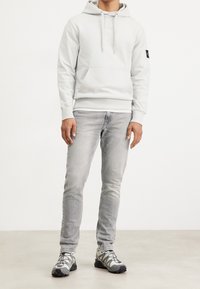 Ljusgrå huvtröja med känguruficka, kombinerad med ljusgrå jeans och grå sneakers med svarta detaljer och snörning.