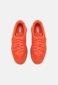 Paire de baskets Puma orange vif avec lacets, détails en mesh et en daim, vue de dessus sur un fond gris clair.