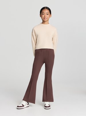 Felpa cropped beige a maniche lunghe abbinata a pantaloni marroni svasati. Completa l'outfit un paio di sneakers bianche con dettagli color granata.