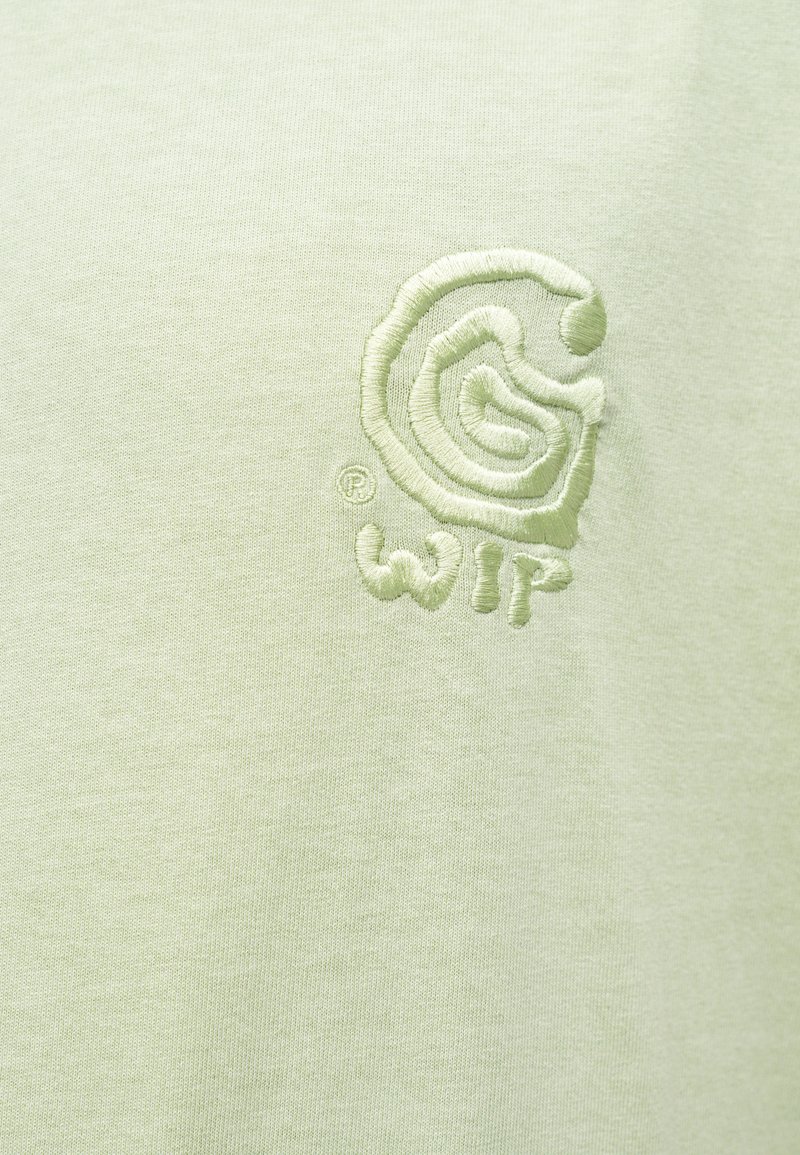Lys grøn bomuld t-shirt med broderet logo i et cirkulært design og tekstureret skrift. Glat stof med minimalistisk æstetik.