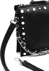 Borsa a mano in pelle nera con rivetti in metallo argentato e dettagli in catena. Ha una chiusura con zip e una tracolla removibile. Superficie testurizzata.