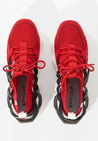 Par de zapatillas de punto rojas Spyder con acentos negros, suelas blancas y cordones rojos, vistas desde arriba sobre un fondo blanco.