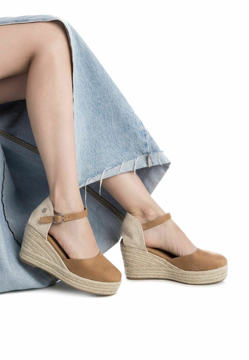 Sandalias de cuña de gamuza marrón con suelas de yute trenzado y detalles de tela a cuadros. La correa ajustable en el tobillo mejora el ajuste.