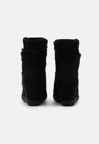 Bottines en daim noir avec un design décontracté, dotées de fermetures éclair sur les côtés et d'un talon compensé pour plus de hauteur.