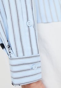 Ljusblå bomullsskjorta med vertikala svarta ränder, försedd med knäppning vid ärmkapen och skräddarsydd passform. Inkluderar en klassisk krage och ren sömnad.