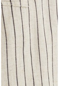 Tissu beige avec des fines rayures verticales noires espacées uniformément et une couture visible près du coin supérieur gauche.
