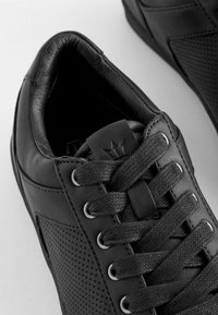 Czarne sneakersy z skórzanymi i perforowanymi panelami, okrągłymi sznurowadłami, metalowymi oczkami i akcentem logo na języku.