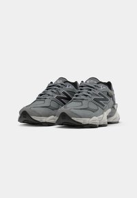 Ein Paar graue New Balance 9060 Sneaker mit schwarzen und weißen Akzenten, nebeneinander auf einem weißen Hintergrund präsentiert.
