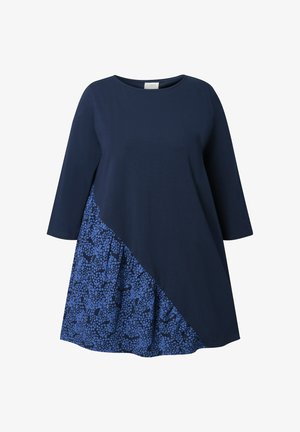 Námořnické modré šaty s tříčtvrtečními rukávy, které mají asymetrický design a vzorovanou modrou látkovou panel na dolním levém rohu.