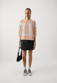 Mnohobočná patchwork blúzka s nafúknutými rukávmi, skombinovaná s čiernou denimovou sukňou. Doplnky zahŕňajú malú čiernu kabelku a šedé tenisky.