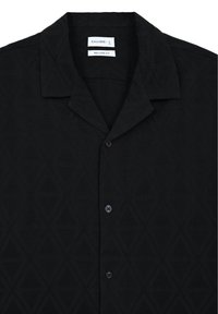 Camicetta nera a maniche corte con motivo a diamante, caratterizzata da colletto a camicia, vestibilità rilassata e chiusura a bottoni frontale.