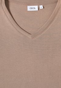 Beige puuvillane V-kaelusega T-särk, millel on peen tekstuur ja õmmeldud kaelus. Sildid näitavad brändi "CECI" ja suurust "S."