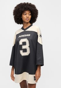 Υπερμεγέθη μαύρη και μπεζ φανέλα από πλεκτό ύφασμα, με μεγάλο αριθμό "3" και το λογότυπο της Adidas σε εμφανές σημείο.
