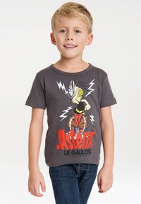 T-shirt in cotone grigio con un personaggio dei cartoni animati e fulmini, e il testo "Asterix Le Gaulois" in rosso e nero. Maniche corte.