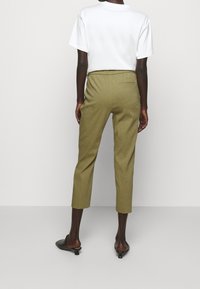Olijf groene cropped broek met een elastische tailleband, voorzien van een enkele achterzak. Gecombineerd met een eenvoudige witte t-shirt en zwarte schoenen.