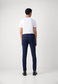 Mornarske hlače krojene u slim fit stilu, u kombinaciji s bijelim majicom s kragnom. Hlače imaju petlje za remen i stražnje džepove. Crne cipele.