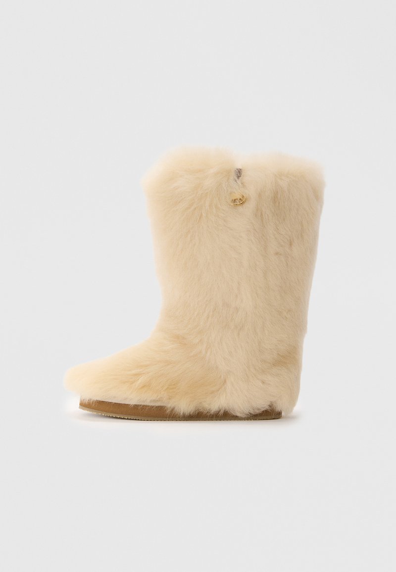 Fodrad beige stövel med en mjuk textur, rund tå och kort skaft. Har en diskret gulddetalj på sidan och en platt sula.