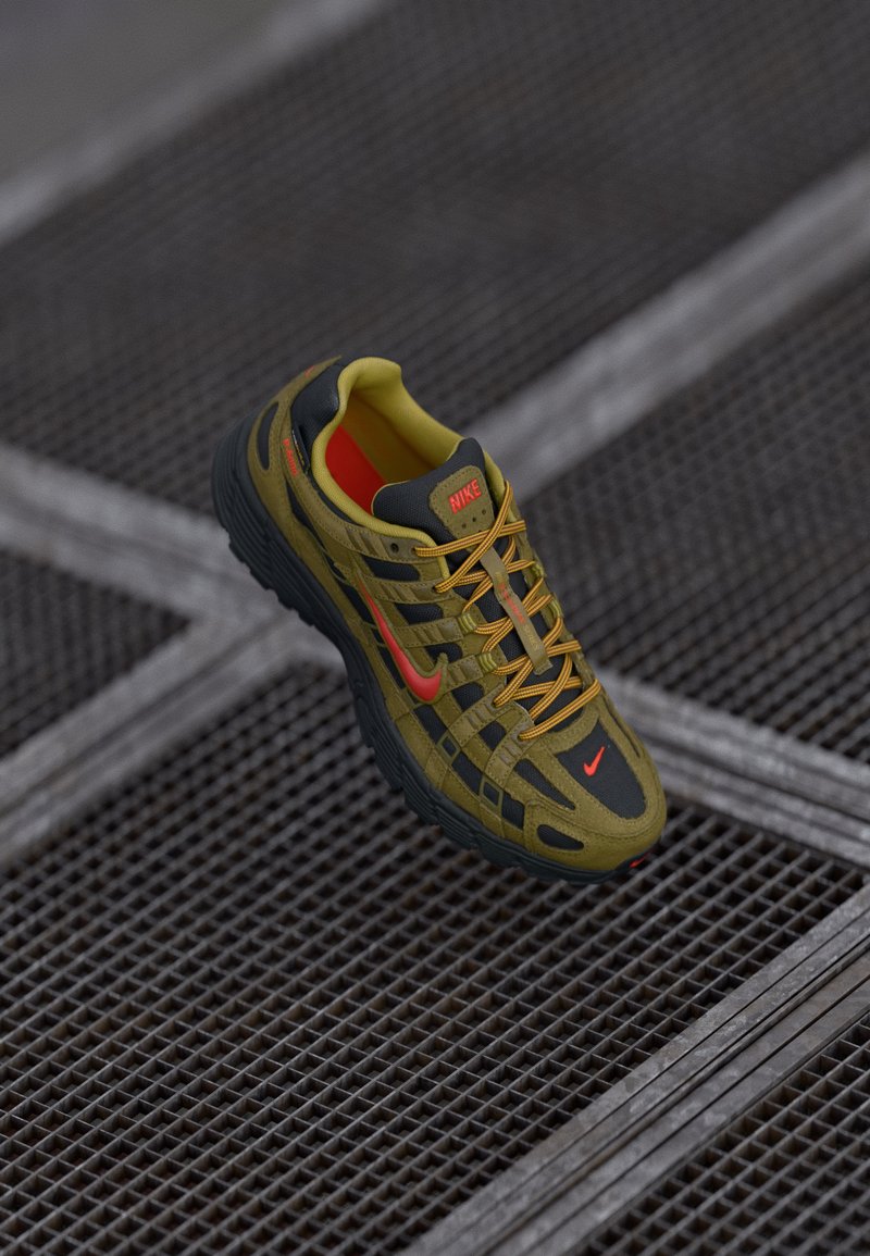 Nike sporta apavi olīvzaļā un melnā krāsā ar spilgti oranžiem akcentiem. Ietver teksturētu dizainu un sieta paneļus gaisa caurlaidībai.