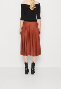 Černý top s odhalenými rameny ve spojení s plisovanou midi sukní v barvě rezavé oranžové. Přiléhavý střih kontrastuje s volně padající sukní. Černé členkové boty.