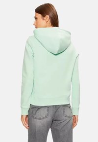 Felpa verde menta con cappuccio a cordino, maniche lunghe e un tessuto morbido e testurizzato. Presenta una tasca a marsupio e polsini a costine.