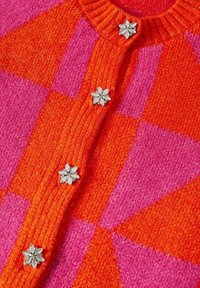 Cardigan en maille à carreaux orange et rose avec bord-côtes et cinq boutons argentés en forme de fleur sur le devant.