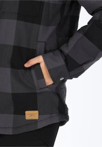Giacca a quadri nera e grigia con tasca sul lato sinistro. Presenta un'etichetta in pelle con la scritta "SWEDMOUNT" sull'orlo inferiore. Texture liscia.