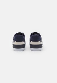Zapatillas de deporte azul marino con textura de punto y talón acolchado. Detalles en gris claro en la entresuela y suela de goma blanca en contraste.