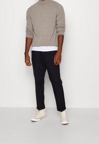 Beżowy sweter z golfem nałożony na białą koszulę, zestawiony z czarnymi rurkowymi spodniami i kremowymi trampkami. Gładka tekstura, dopasowany krój.