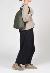 Mochila verde oliva con un diseño sencillo, cuenta con correas ajustables y una textura suave. Se lleva con un suéter ligero y pantalones anchos.